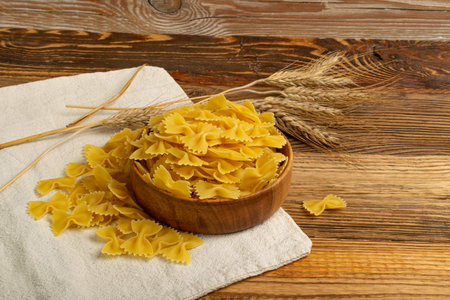 Raw Farfalle Pasta on Wooden Table, Yellow Dry Butterfly Noodles, Wheat Bow Macaroni, Uncooked Farfalle in Bowl on Wood Rustic Background Side Viewの写真素材