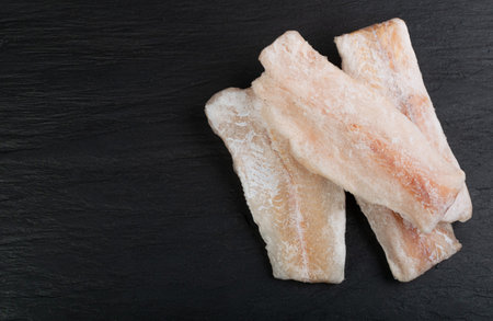 Frozen Fish on Black Plate, White Cod Fillet, Iced Hake Filet, Frozen Pollock Meat on Dark...