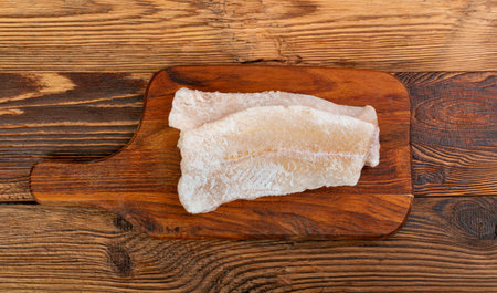 Frozen Fish on Wooden Cutting Board, White Cod Fillet, Iced Hake Filet, Frozen Pollock Meat on Rustic Wood Background Top Viewの写真素材