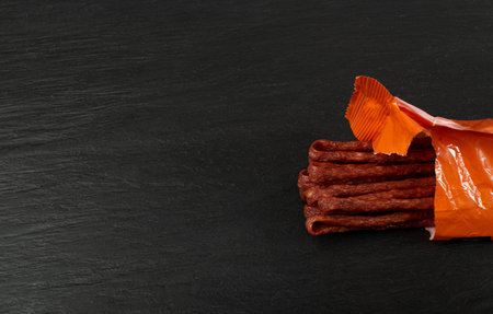 Dried Smoked Sausage, Thin Salami Sticks, Cabanossi, Kabanos, Dry Embutido, Thin Bratwurst Sausage on Black Stone Backgroundの写真素材