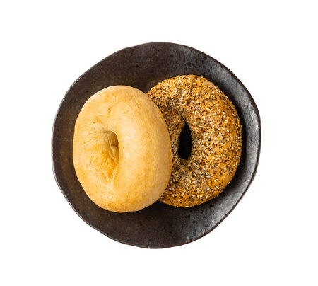 Bagel Isolated, Two Round Bread Buns, Wheat Bakery with Grains And Seeds for Breakfast, Plain Circle Bagels Bread on Black Plate on White Backgroundの写真素材