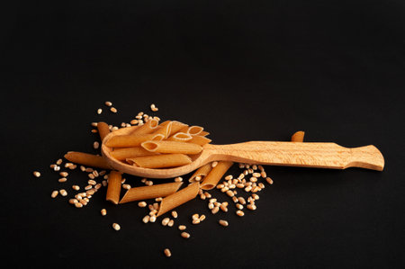 Raw Brown Pasta, Wholegrain Penne Pile in Spoon, Dry Whole Grain Noodle, Raw Spelt Macaroni, Healthy Italy Food, Organic Meal, Wholewheat Pasta on Black Backgroundの写真素材