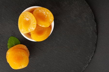 Canned Peaches in Bowl, Apricot Halves in Syrup, Yellow Fruit Dessert, Tinned Nectarine Compote, Orange Peeled Peache Slices on Black Backgroundの写真素材
