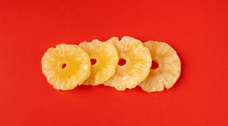 Dry Pineapple Rings Isolated, Candy Pineapples, Dehydrated Yellow Sugar Fruit, Candied Fruits Circles, Dry Pineapple on Red Backgroundの写真素材
