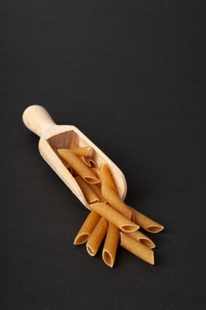 Raw Brown Pasta, Wholegrain Penne Pile in Scoop, Dry Whole Grain Noodle, Raw Spelt Macaroni, Healthy Italy Food, Organic Meal, Wholewheat Pasta on Black Backgroundの写真素材