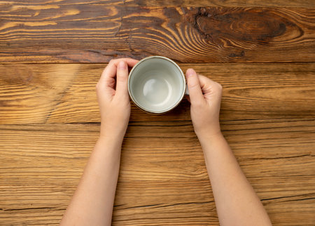 Hand Holds Cup, Empty Cup in Hands, Coffee Mug, Teacup, Hot Beverage Mockup, Gray Cup in Arms on Wooden Table, Rustic Background with Copy Space for Text Top Viewの写真素材