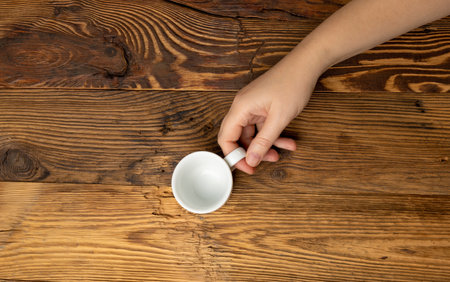 Hand Holds Cup, Empty White Cup in Hands, Coffee Mug, Teacup, Hot Beverage Mockup, Cup in Arms on Wooden Table Background with Copy Space for Text Top Viewの写真素材