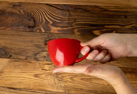 Hand Holds Cup, Empty Red Cup in Hands, Coffee Mug, Teacup, Hot Beverage Mockup, Cup in Arms on Wood...
