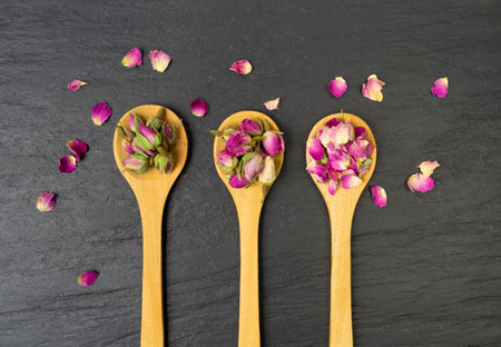 Dry Rose Buds, Roses Petals for Pink Flower Tea, Dried Persian Rosebuds, Rose Buds Textured Flowers in Wooden Spoon on Black Stone Plate Backgroundの写真素材