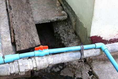 Blue PVC valve red handle connecting blue PVC pipe fitting, blue PVC elbow 90 degree and blue PVC reducing socket pipe stay near steel water piping closeup.の写真素材