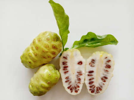 Morinda citrifolia fruits and two halves slice with green leaves isolated on white background closeup.の写真素材
