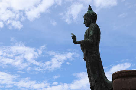 Left of Buddha statue is standing isolated on blue sky and white cloud background closeup at Phutthamonthon park, Nakhon Pathom,Thailand.のeditorial素材