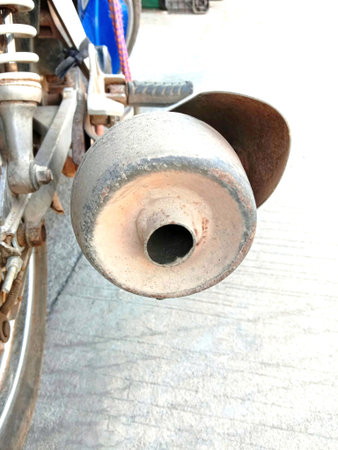 Motorcycle end exhaust pipe at frame on blurred cement flooring closeup.
