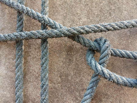 Old nylon ship ropes tied to knot bound around cement electrical post on ground flooring closeup.の写真素材