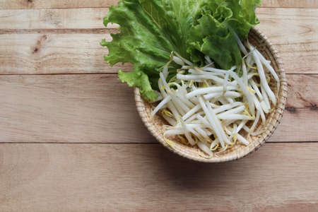 Vegetables and sprouts in the wicker basket with copy space isolated on wooden background closeup.の写真素材