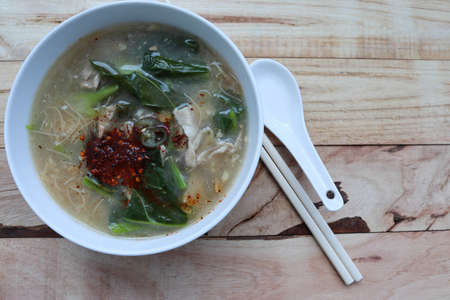 Fried soup noodles, Pork, and Kale with sauce in the bowl, spoon, chopsticks, delicious food Thai people called "Rad Na" isolated on wooden background closeup.の写真素材