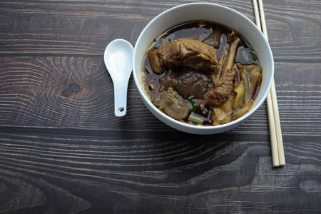 Duck noodles in the bowl with a spoon and chopsticks isolated on wooden wallpaper background closeup.の写真素材