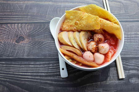 Yentafo noodles, red sauce, fish ball with spoon and chopsticks in white bowl, Thai delicious food isolated on wooden wallpaper background closeup.の写真素材
