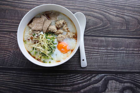 Congee, Rice soup, Rice porridge with egg in the bowl and spoon, Thai morning delicious food isolated on wooden wallpaper background closeup.の写真素材