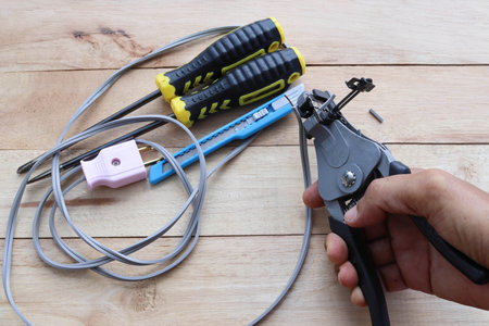 Hand is using wire stripper pliers stripping electric wire and use with various tools isolated on wooden background closeup.の写真素材