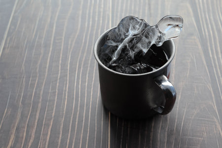 Cup of coffee with ice cubes on wooden table, closeup