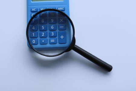 Magnifying glass and calculator on light blue background, top view. Space for textの写真素材