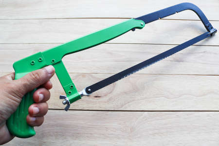 Hands are holding a hacksaw on a wooden background. The concept of repair and constructionの写真素材