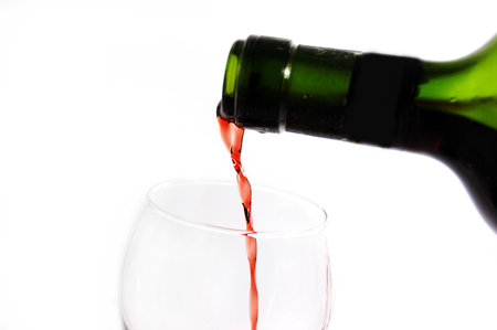 Green bottle pouring red wine into wineglass over white