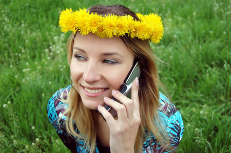 Blonde happy girl with dandelion diadem talking on phoneの写真素材