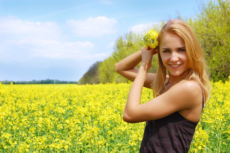 Beautiful girl among blooming raps field with flower