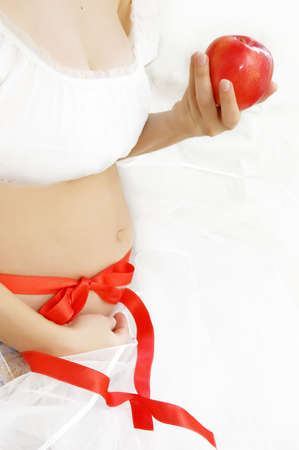 Woman hands holding pregnant belly over white with red apple and ribbonの写真素材