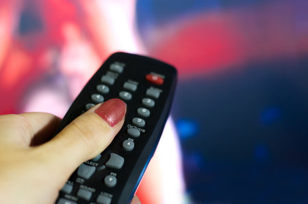 Hand holding remote control pointing to blurred TV program