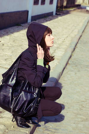 Sad brunette with hood on the pavement edgeの写真素材