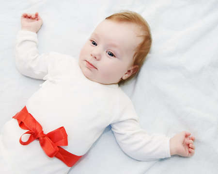 Adorable baby boy in light with red ribbon as giftの写真素材