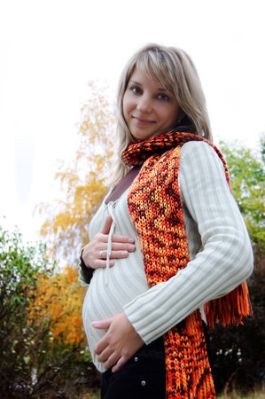 Smilng pregnant woman in autumn park with scarfの写真素材