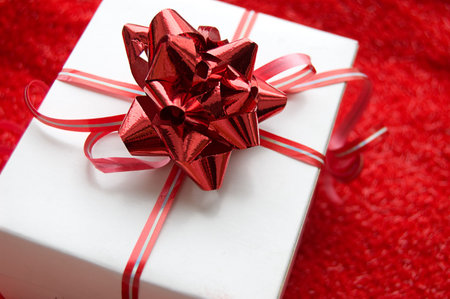 White gift box with red satin ribbon on red background