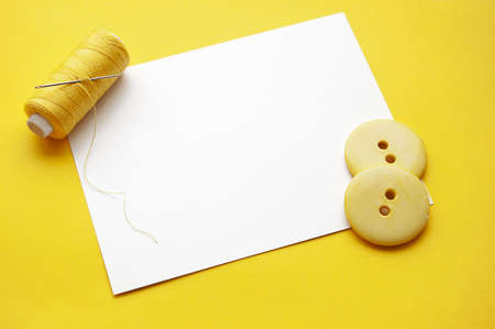 Yellow thread, needles and some buttons on blank noteの写真素材