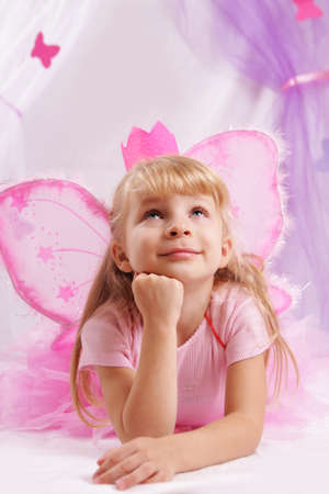 Little princess girl in pink crown and butterfly wings making wishesの写真素材