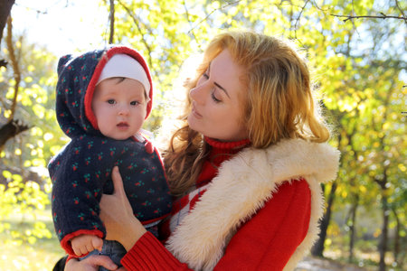 Happy mother and baby girl talking in autumn park