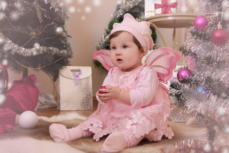Angel like baby girl with pink butterfly wings sitting under Christmas treeの写真素材