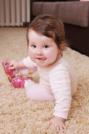 Cute baby girl showing tongue and sitting on carpet