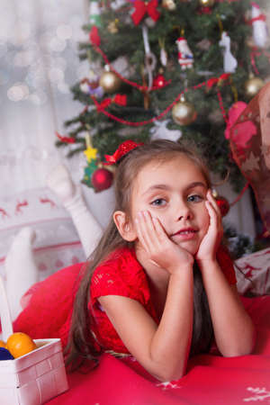 Beautiful girl in red lying under Christmas treeの写真素材