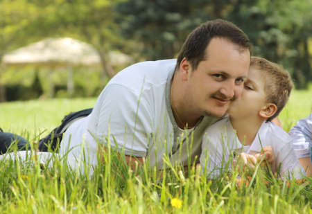 Son kissing his father among green grassの写真素材