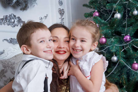 Two kids cheek to cheek with their mother under Christmas treeの写真素材