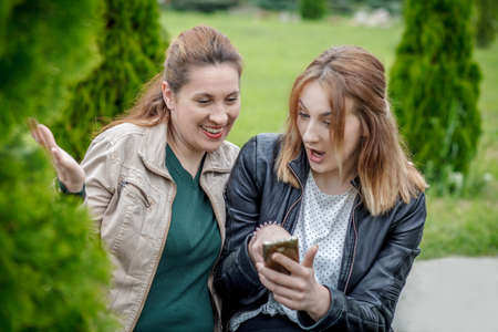 Two amazed women friends sharing social media in smart phone outdoorsの写真素材