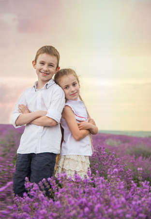 Happy brother and sister in lavender summer field back-to-backの写真素材