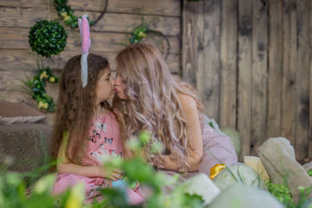 Little child girl wearing bunny ears kissing her mother among Easter decoration in studioの写真素材