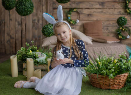 Funny portrait of girl having fun on Easter wearing bunny ears and holding eggs on eyes during spring seasonの写真素材