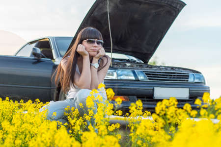 Girl is bored near the broken car on the meadowの写真素材
