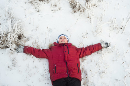 Boy in red jacket bright lying in the snow with a smileの写真素材
